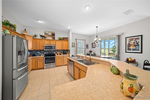 kitchen with appliances with stainless steel finishes, sink, light tile patterned floors, a notable chandelier, and hanging light fixtures