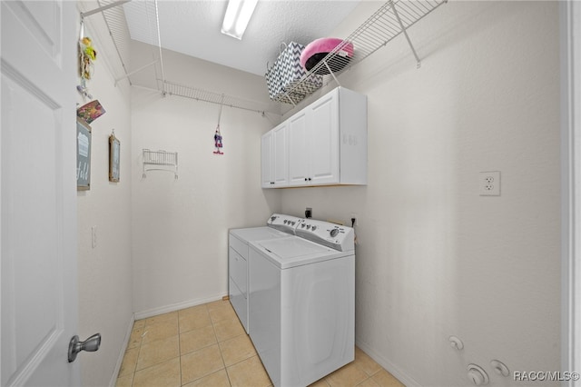 laundry area with washing machine and clothes dryer, light tile patterned floors, and cabinets