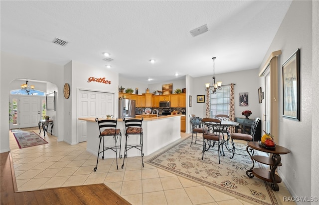 kitchen featuring appliances with stainless steel finishes, light tile patterned floors, pendant lighting, a notable chandelier, and a center island