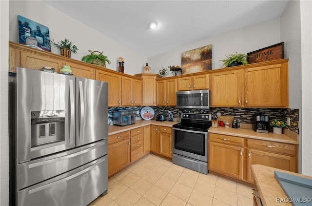 kitchen featuring vaulted ceiling, light tile patterned floors, a textured ceiling, appliances with stainless steel finishes, and tasteful backsplash