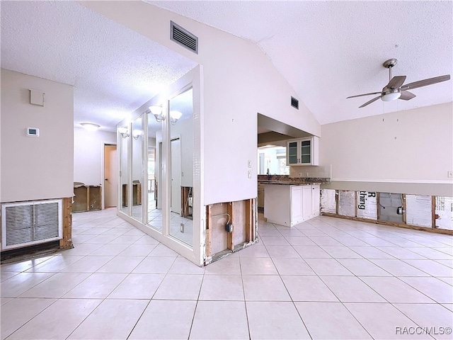 interior space featuring vaulted ceiling, light tile patterned floors, white cabinets, and a textured ceiling