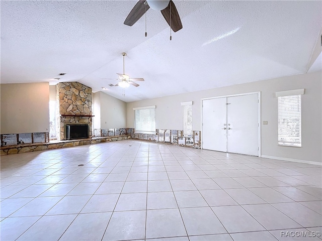 unfurnished living room with light tile patterned floors, ceiling fan, a textured ceiling, a stone fireplace, and vaulted ceiling