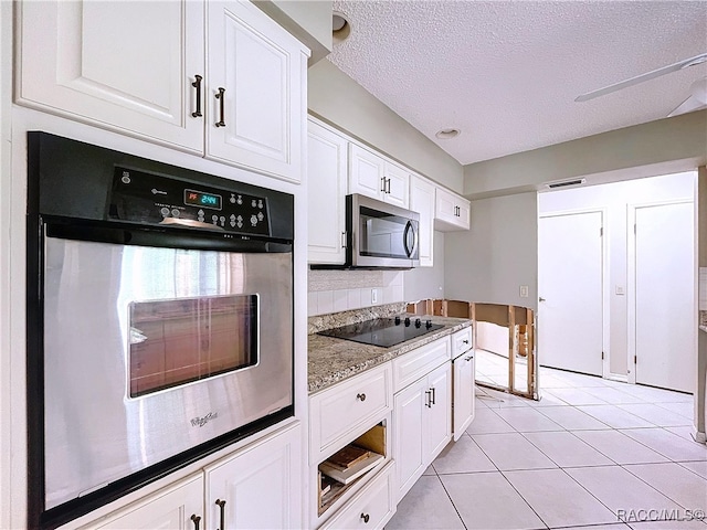 kitchen with a textured ceiling, light tile patterned floors, appliances with stainless steel finishes, dark stone counters, and white cabinets