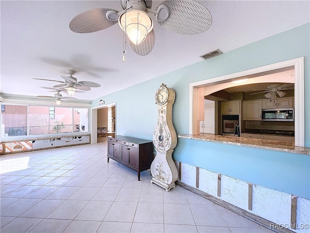 unfurnished living room featuring light tile patterned flooring, ceiling fan, and a textured ceiling