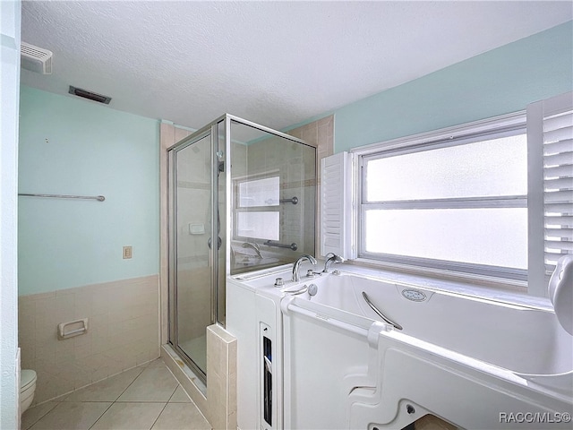 bathroom featuring tile patterned flooring, tile walls, a textured ceiling, independent shower and bath, and toilet