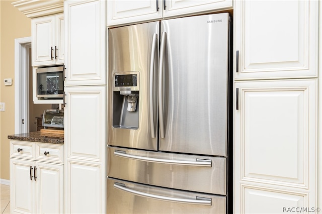 kitchen with white cabinets, stainless steel appliances, light tile patterned flooring, and dark stone countertops