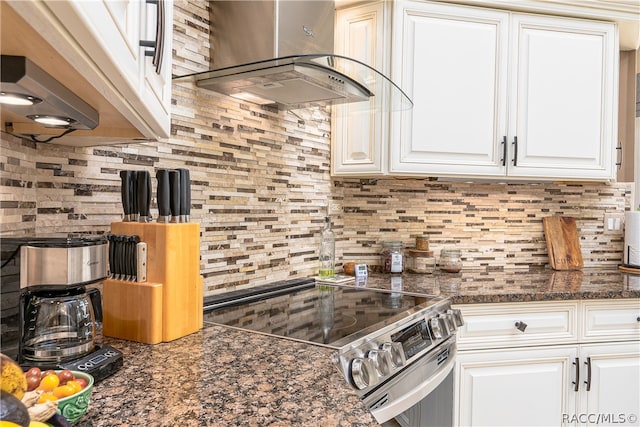 kitchen with tasteful backsplash, electric stove, wall chimney range hood, dark stone countertops, and white cabinets