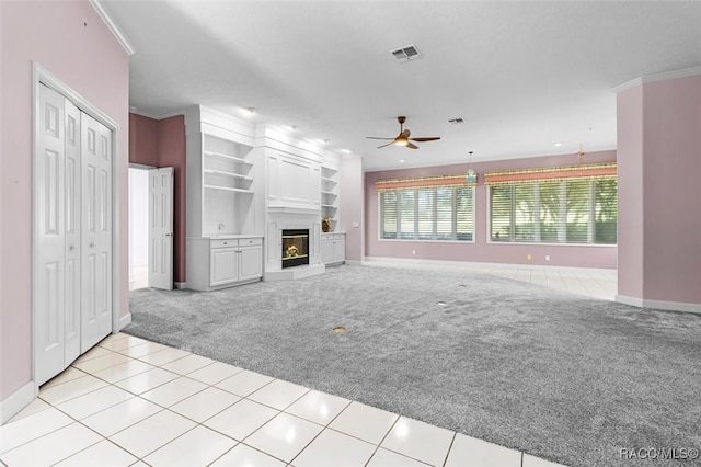 unfurnished living room with built in shelves, light colored carpet, ceiling fan, and ornamental molding