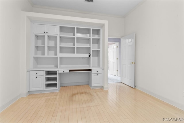 unfurnished office featuring light hardwood / wood-style flooring, built in desk, and ornamental molding