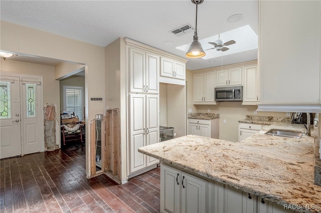 kitchen with light stone counters, ceiling fan, dark wood-type flooring, sink, and decorative light fixtures