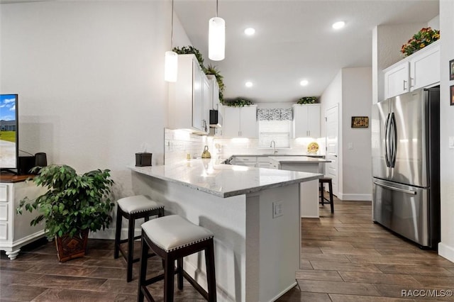 kitchen featuring wood finish floors, a peninsula, a breakfast bar, and freestanding refrigerator