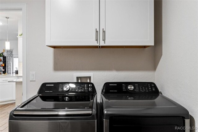 clothes washing area with cabinet space, wood finished floors, and washing machine and dryer