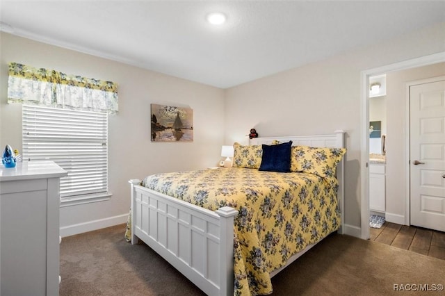 bedroom with dark colored carpet, baseboards, and ensuite bath