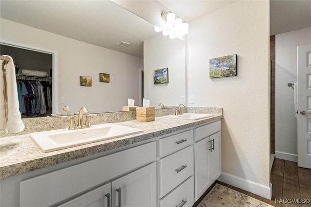 bathroom with a sink, baseboards, a spacious closet, and double vanity