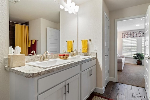 ensuite bathroom featuring double vanity, connected bathroom, wood tiled floor, and a sink