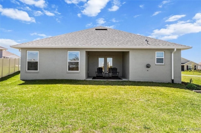 rear view of house with a shingled roof, a yard, and fence