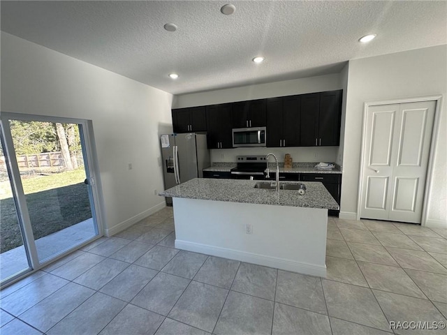 kitchen featuring sink, light stone counters, a center island with sink, light tile patterned floors, and appliances with stainless steel finishes