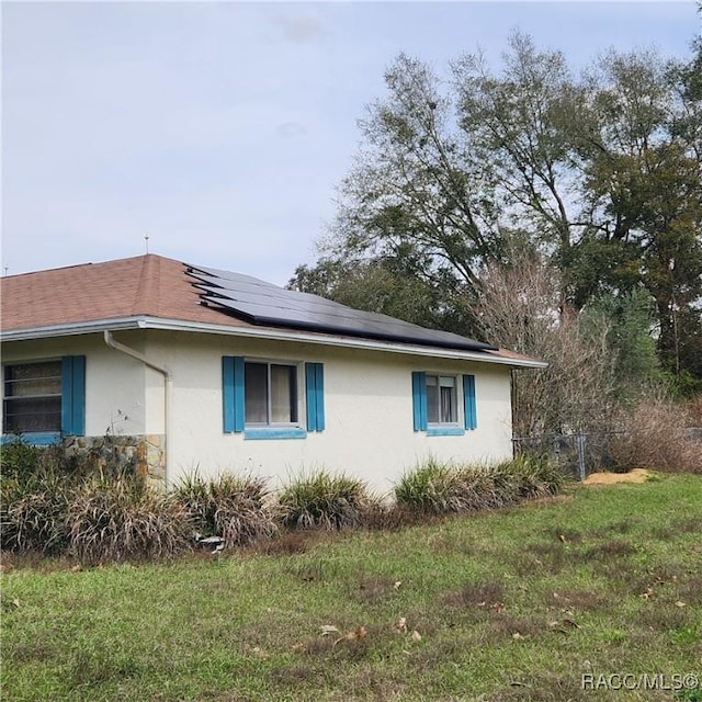 view of home's exterior with stucco siding, a lawn, and solar panels