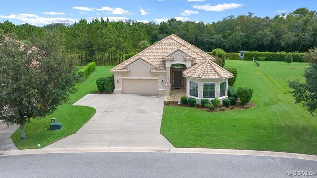 mediterranean / spanish house featuring a garage, driveway, a front lawn, and a tiled roof