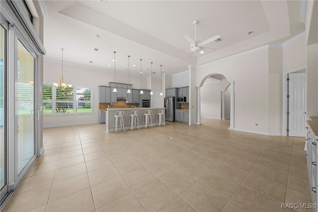 unfurnished living room featuring a raised ceiling, light tile patterned floors, arched walkways, and ornamental molding