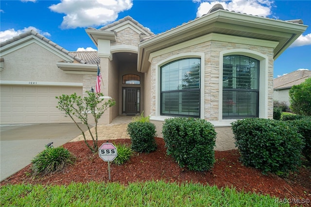 mediterranean / spanish-style home with stucco siding, concrete driveway, a garage, stone siding, and a tile roof