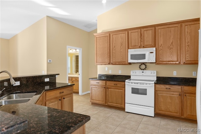 kitchen with lofted ceiling, white appliances, dark stone counters, sink, and light tile patterned flooring