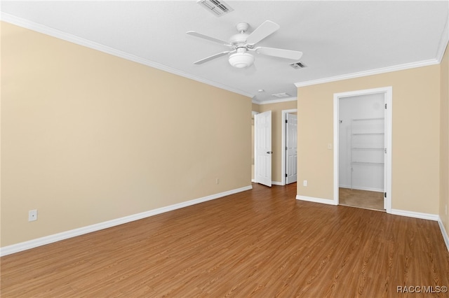 unfurnished bedroom featuring ceiling fan, wood-type flooring, a walk in closet, and ornamental molding