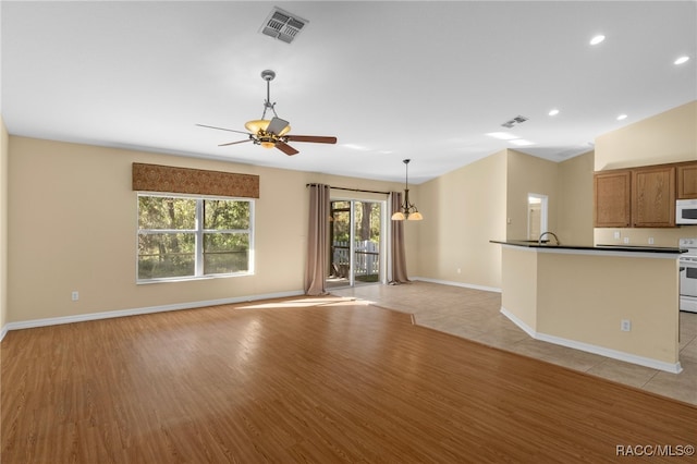 unfurnished living room featuring ceiling fan with notable chandelier, vaulted ceiling, and light hardwood / wood-style flooring