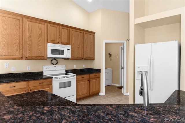 kitchen featuring washer / dryer, white appliances, dark stone countertops, and light tile patterned floors