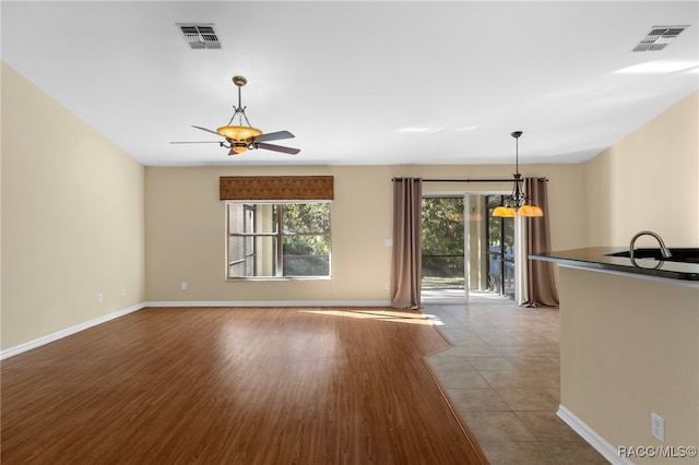 unfurnished living room featuring light hardwood / wood-style flooring and ceiling fan with notable chandelier