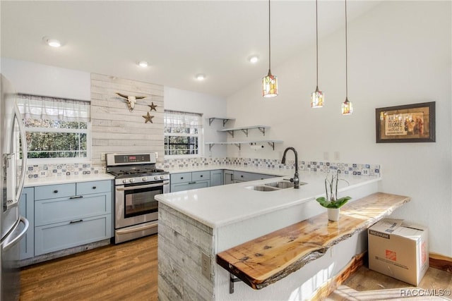 kitchen with sink, kitchen peninsula, decorative light fixtures, appliances with stainless steel finishes, and hardwood / wood-style flooring