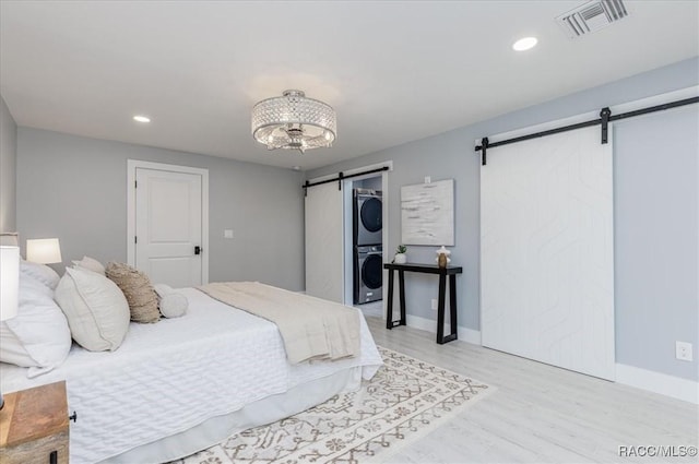 bedroom with light hardwood / wood-style floors, a barn door, and stacked washing maching and dryer