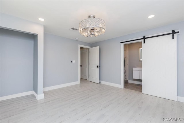 unfurnished bedroom featuring ensuite bathroom, a barn door, and light hardwood / wood-style floors