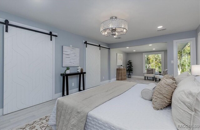 bedroom with light hardwood / wood-style flooring, an inviting chandelier, and a barn door