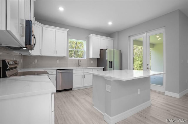 kitchen featuring backsplash, appliances with stainless steel finishes, a center island, a sink, and light wood-style floors