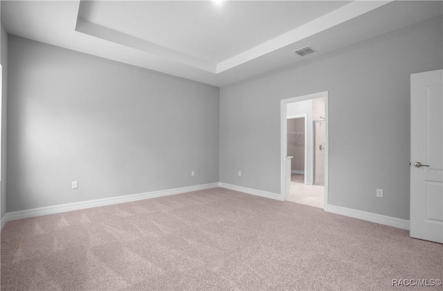 unfurnished room featuring visible vents, baseboards, a tray ceiling, and light carpet