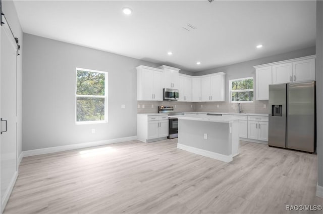 kitchen featuring light countertops, decorative backsplash, appliances with stainless steel finishes, and a barn door