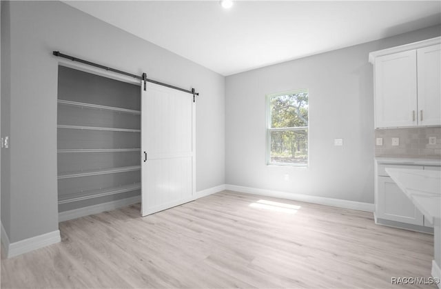 interior space featuring baseboards, a barn door, and light wood finished floors
