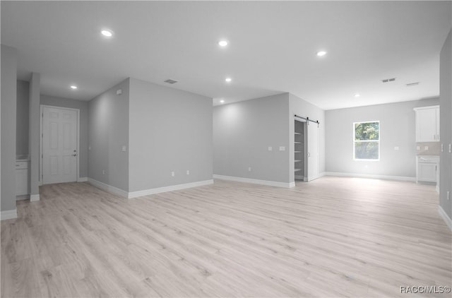 unfurnished living room featuring recessed lighting, a barn door, and light wood-style floors