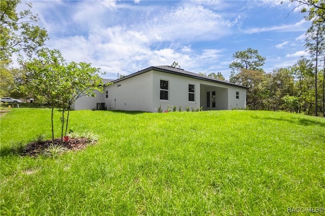 rear view of house featuring a lawn, stucco siding, and cooling unit