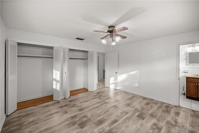 unfurnished bedroom with ensuite bathroom, ceiling fan, multiple closets, and light hardwood / wood-style flooring