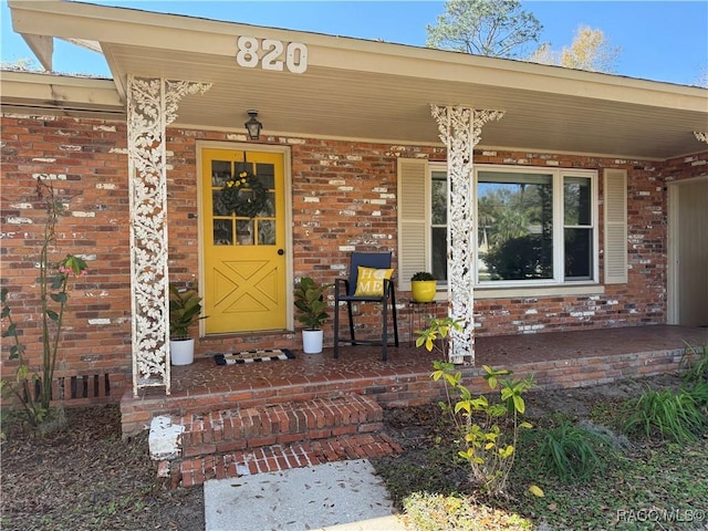 entrance to property featuring a porch and brick siding