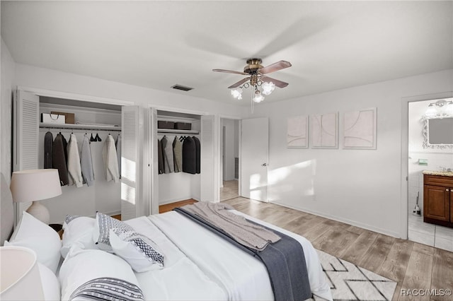 bedroom featuring ceiling fan, two closets, ensuite bath, and light wood-type flooring