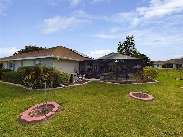 back of house featuring solar panels, a lanai, and a lawn