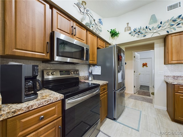 kitchen featuring decorative backsplash, light tile patterned floors, light stone counters, and appliances with stainless steel finishes