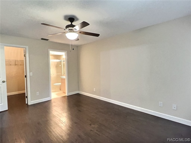 unfurnished bedroom with ceiling fan, a spacious closet, connected bathroom, dark hardwood / wood-style floors, and a closet