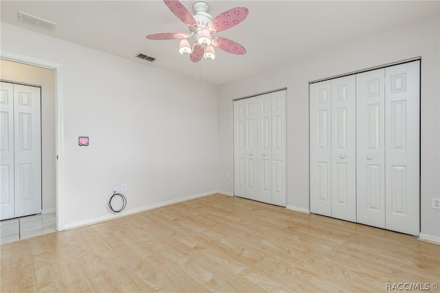 unfurnished bedroom featuring ceiling fan, light hardwood / wood-style floors, and multiple closets