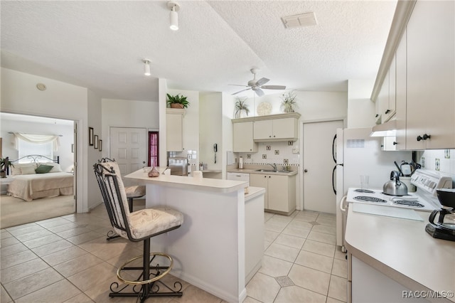 kitchen featuring light tile patterned floors, a ceiling fan, white electric stove, light countertops, and a kitchen bar