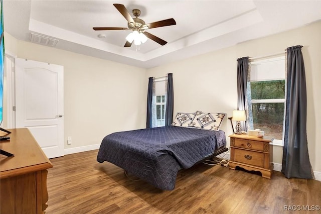 bedroom featuring baseboards, visible vents, a raised ceiling, ceiling fan, and wood finished floors