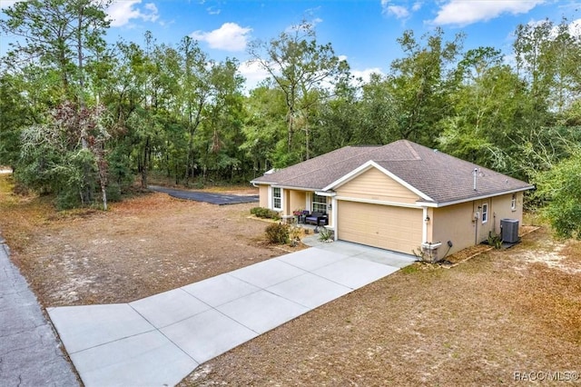 ranch-style house with an attached garage, central air condition unit, a shingled roof, driveway, and stucco siding